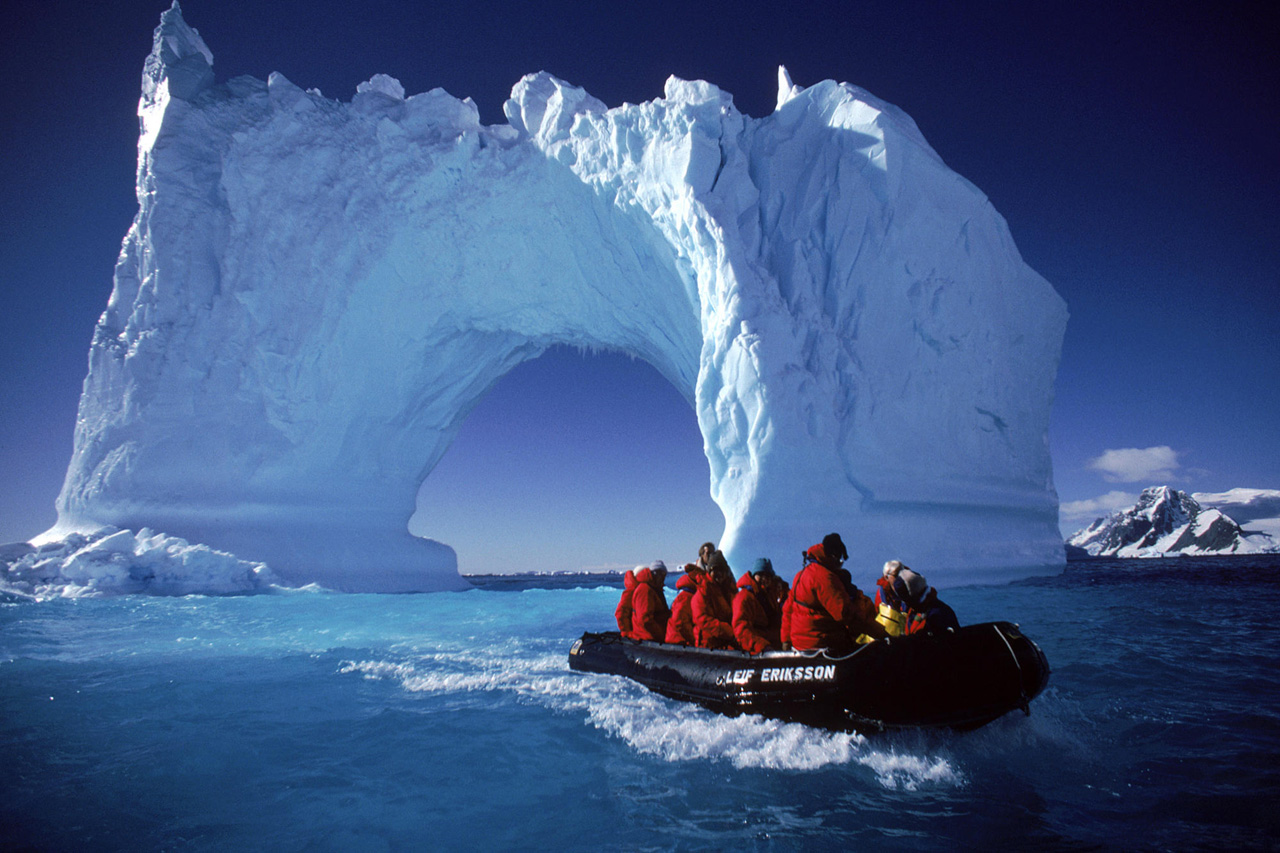 Boating by an iceberg arch near Yalour Islands, Antarctica.